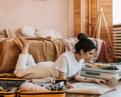 Femeie pregatind bagajele pentru vacanta si uitandu se pe harta