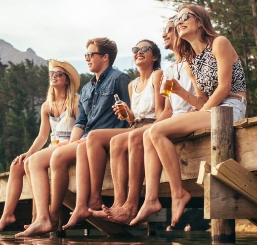 grup de tineri sarbatoresc weekendul la munte pe un pod la marginea unui lac