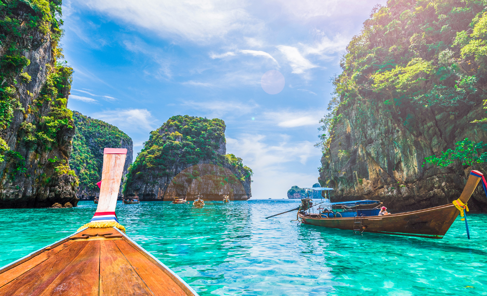 Decor de vis in Thailanda, barca traditionala intre stanci, plaja fina si apa de un albastru turcoaz.